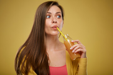 Fototapeta premium Young woman drinking orange juice from bottle with straw looking up. Close up face. Isolated advertising portrait on yellow.