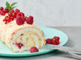 Baked meringue roll with red berries on a round plate, white background