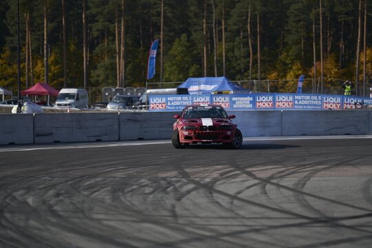 11-05-2022 Riga, Latvia A Red Car Driving Down A Race Track, A Car In A Race Track On One Side And Another Driving Away Behind It.