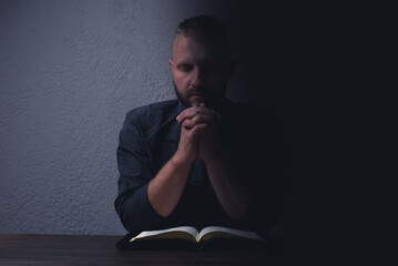 A man sits at a table and reads the Holy Bible. Pray with folded hands. Prayer and hope to God