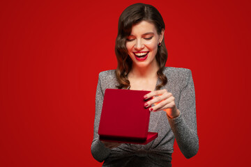 Happy surprised woman in party dress opening present box on red background