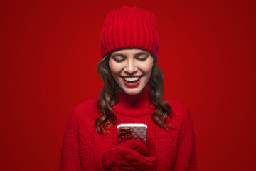 Surprised woman holding phone browsing social media wearing mittens on red background