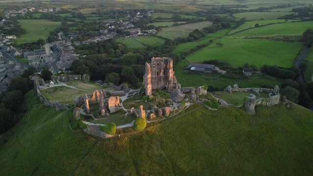 4k drone footage of Corfe Castle and village surrounded by green fields. England, UK.