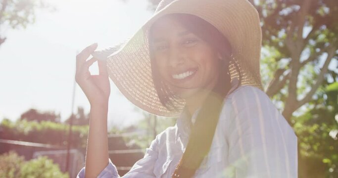 Video portrait of happy biracial woman wearing sunhat in sunny garden smiling to camera