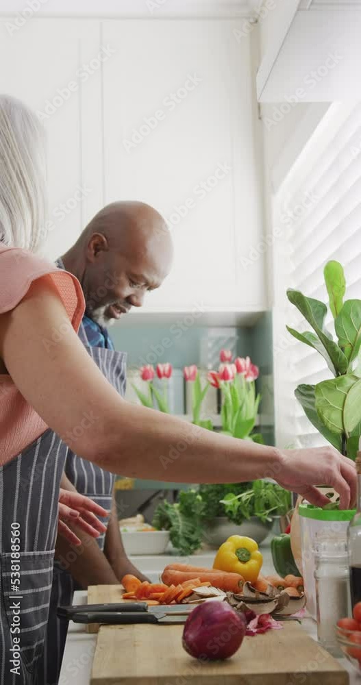 Canvas Prints Vertical video of happy diverse senior couple preparing food and composting vegetables in kitchen