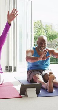 Vertical video of happy diverse senior couple practicing yoga exercising together sitting indoors