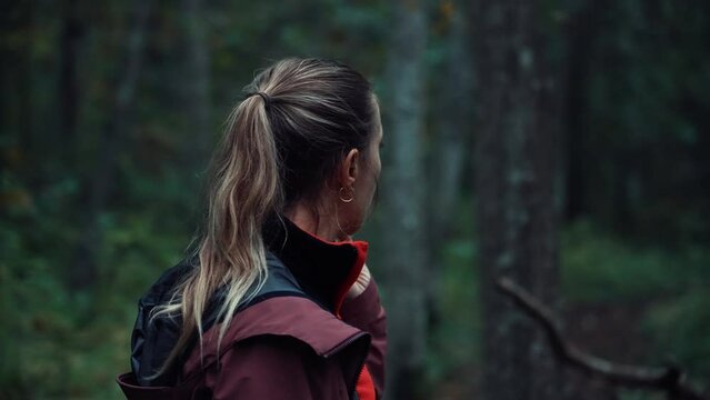 Blonde girl looks around in the forest. Puzzled hiker is worried about the coming twilight. Lost in the woods. Fear, feeling lost, lost the path. Young woman thinks what to do and where to go..