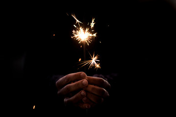 Human people hands holding fire sparkler in black background. Concept of holiday and fun. Hope and future with copy space. Close up. Party event and loneliness. One woman celebrate alone in the dark - Powered by Adobe
