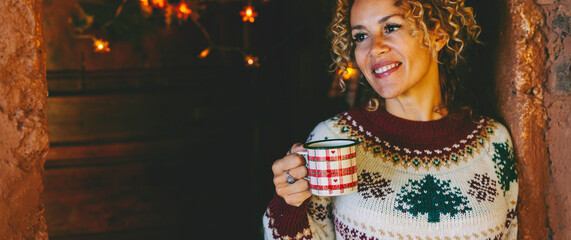 Horizontal portrait of attractive middle age woman smiling and taking tea cup in christmas time at...