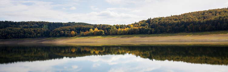 a boat on the german edersee lake with very low water due to climate change in autumn 2022 panorama