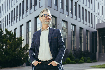 Portrait of senior successful investor, mature businessman outside office building in business suit...