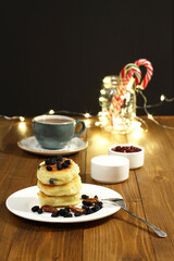 Cheese pancakes lie on a plate, sprinkled with raisins and pecans, and saucers with sour cream and jam stand side by side on a wooden table