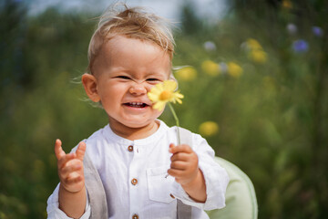 
one year old happy blond german baby boy in white shirt playing outside in the garden with a yellow flower to send love or congratulate for birthday
 - obrazy, fototapety, plakaty