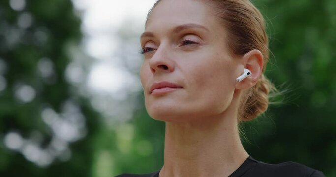 Portrait of woman with earphones meditating with closed eyes standing in the park