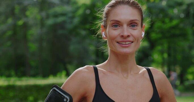 Portrait of fit woman runner standing in the park and smiling into the camera