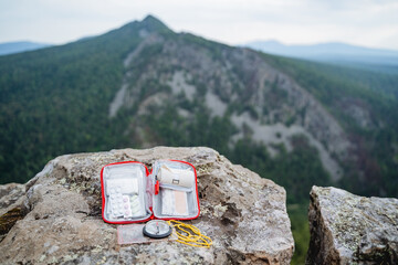 An opened first aid kit lies on a stone high in the mountains, a compass for orientation in the...