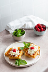 Belgian waffles in a white plate with raspberry mint and whipped cream for breakfast