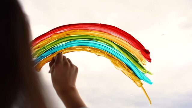 A child draws a rainbow on the glass of a balcony. Drawings with colorful rainbow images alone at home.