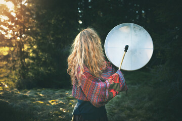Naklejka premium Beautiful shamanic girl playing on shaman frame drum in the nature.Shot from the back.