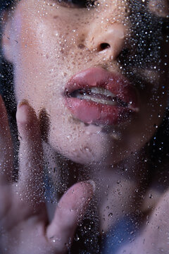 Cropped view of sexy woman touching wet glass on black background.