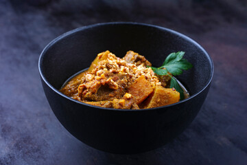 Traditional Indian vegetarian Madras curry stew with sweet potatoes and roasted cashew nuts served as close-up in design bowl with copy space