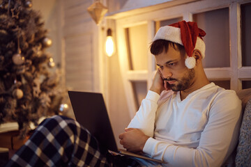 Young bored man using laptop while spending Christmas Eve alone at home.