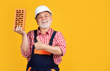happy old aged man bricklayer in helmet on yellow background. thumb up - obrazy, fototapety, plakaty