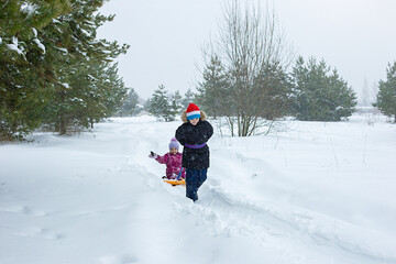 Fototapeta na wymiar A boy rolls a little girl in the snow on a ice rink.