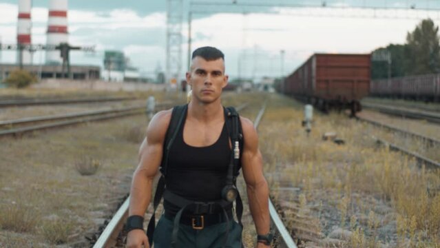 Portrait of handsome young muscular man with balloon dragger on the back who is goes along the rails near the factory. Slow motion