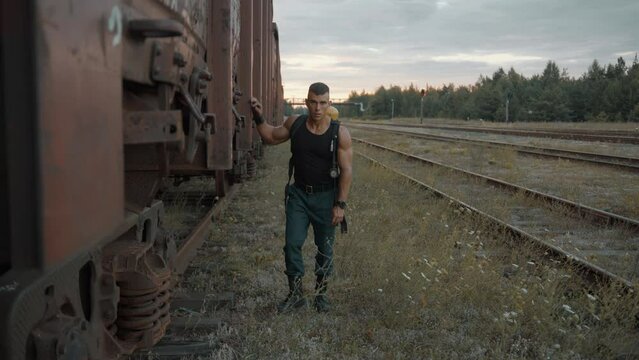 A young muscular man with a balloon drager on his back stands leaning against a freight wagon and then goes forward