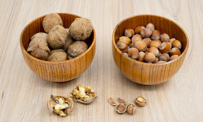 Fototapeta na wymiar Hazelnuts and walnuts in a bowl with a few cracked next to it on the table. 