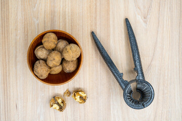 Walnuts in a bowl with a nutcracker next to it on the table. Flat lay.