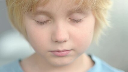Close-up portrait of sad and thoughtful school-age child. The cute boy closed his eyes, then opened them and looks at you very seriously. Upset, offended and lonely kid