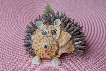 a figurine of a toy hedgehog made of seashells stands on a pink table