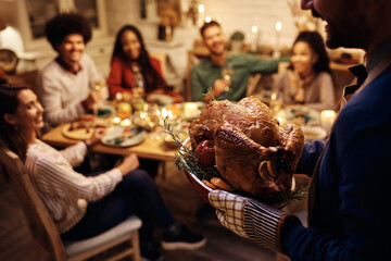 Close up of man serving roasted turkey during Thanksgiving dinner party with friend.
