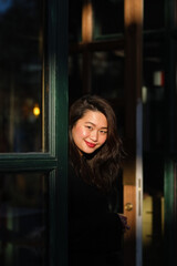 Pretty southeast Asian woman with dark wavy hair and red lips smiles at the camera. Female is outdoors on a beautiful summer day, the sun on her face.
