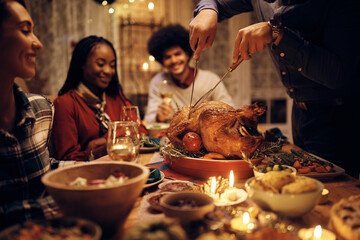 Close up of man carving turkey while having Thanksgiving meal with friends at dining table.