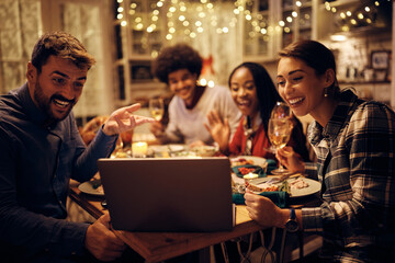 Happy friends making video call during Thanksgiving dinner at dining table.