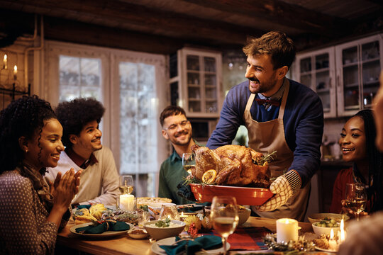 Young happy man serving Thanksgiving turkey to his friends at dining table.