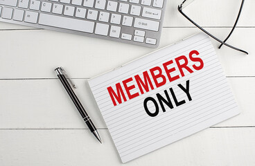 MEMBERS ONLY text on notebook with keyboard , pen glasses on white wooden background