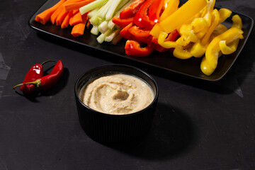 Hummus with vegetables on a dark background