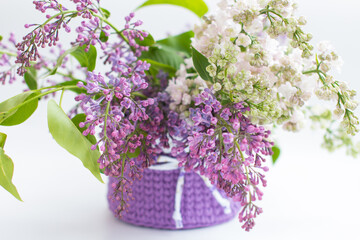 A basket with balls of yarn and a bouquet of lilacs. On a white background