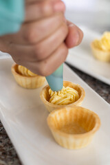 hand of a person holding a kitchen instrument to put cream on bun, food preparation with pastry cream, decoration