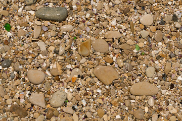Small pebbles form the background of the sea shore. Coarse multicolor sand.