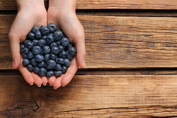 Woman with heap of tasty blueberries on wooden background, top view. Space for text