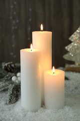 Fototapeta na wymiar Burning candles and Christmas decor on artificial snow