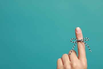 Woman showing index finger with tied bow as reminder on light blue background, closeup. Space for...
