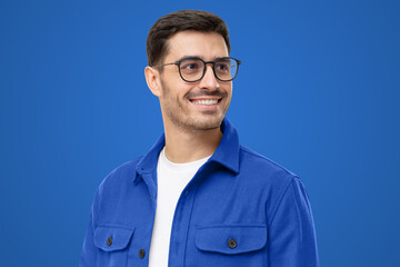 Close-up portrait of young handsome smiling man wearing casual blue shirt and glasses, looking away