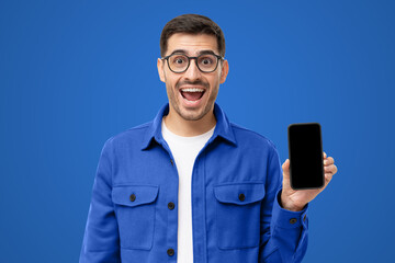 Amazed shocked man showing empty black screen of phone in hand, isolated on blue