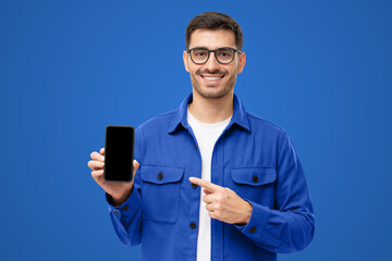 Handsome man in blue shirt presenting smart phone and pointing with finger at blank black screen